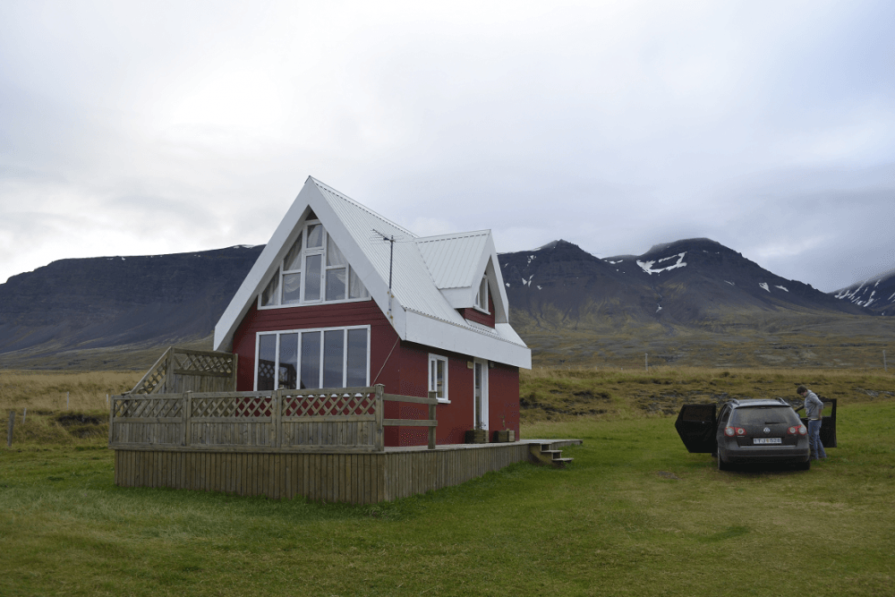Small cabin in a grassy area in Iceland, with mountains in the background and a car parked alongside.