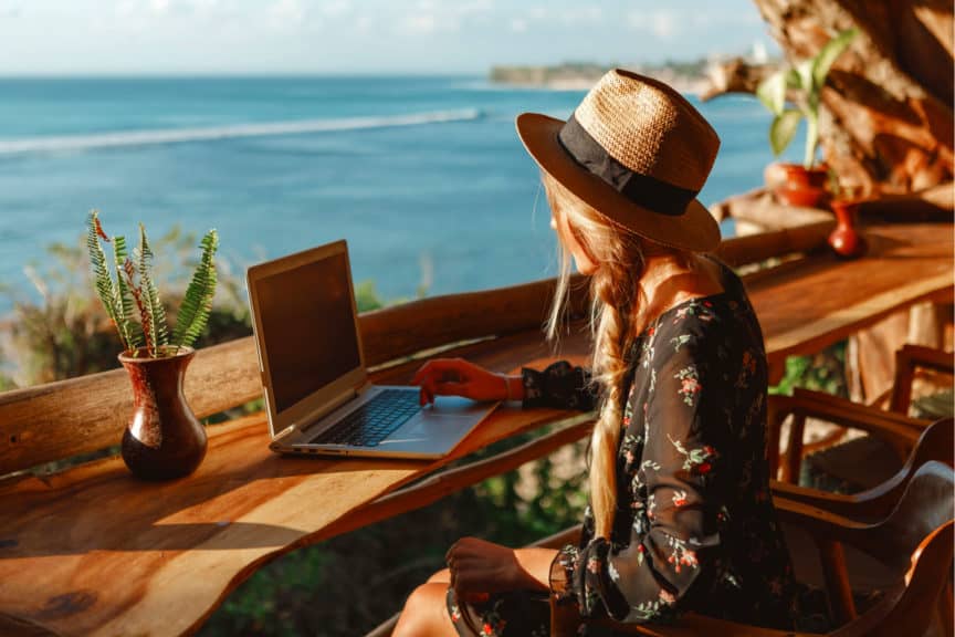 Woman using laptop at outdoor table overlooking ocean