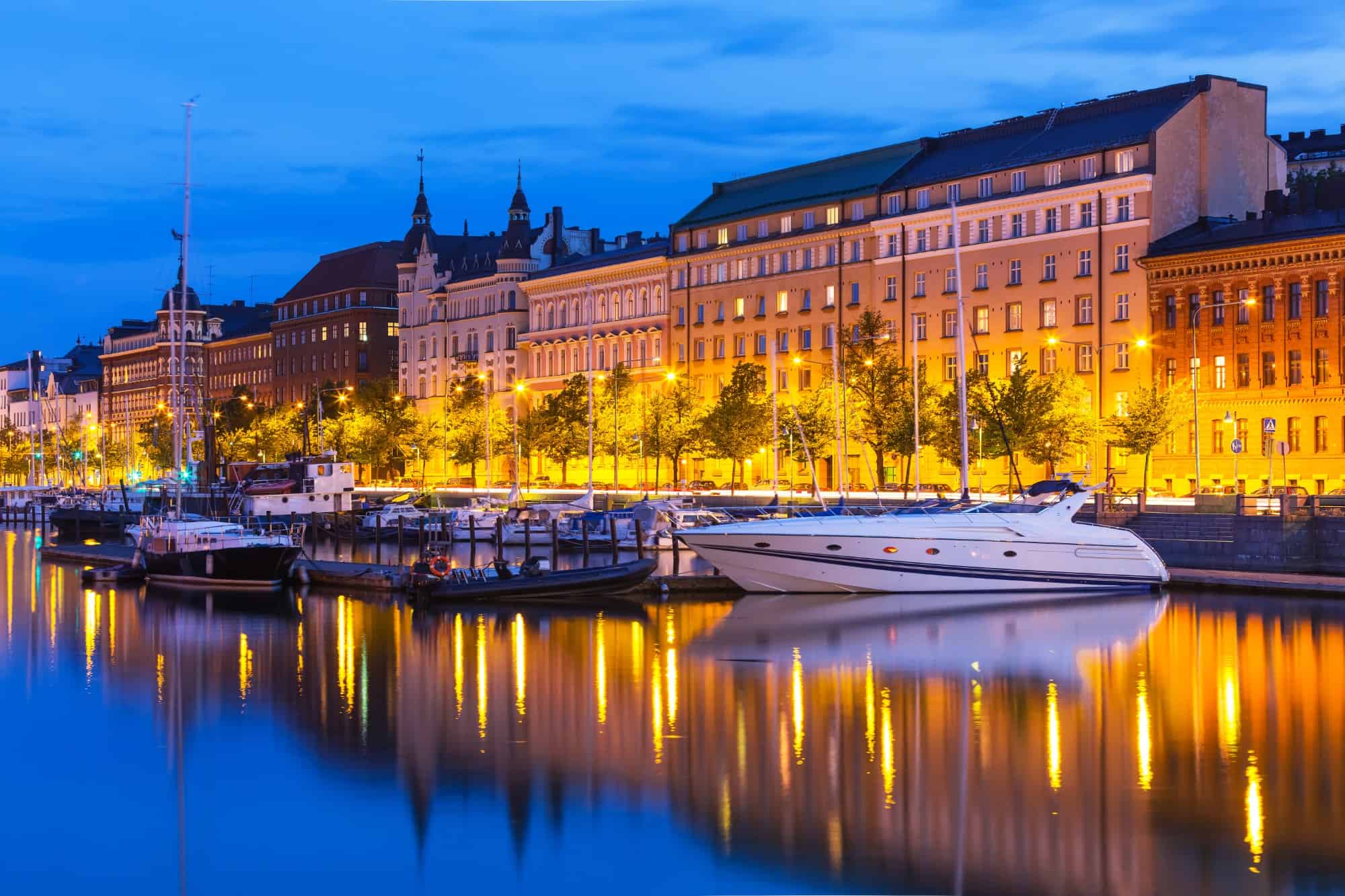 Yachts in harbor in Helsinki with grand buildings in background, at sunset