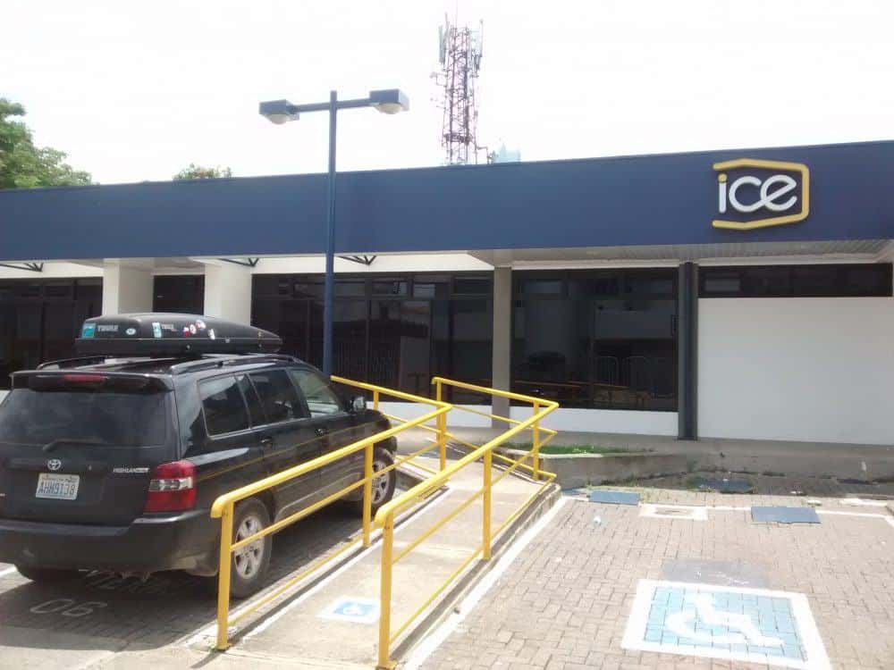 ICE electric company branding on a store in Costa Rica. Car is parked outside the building. A cell phone tower is visible behind.