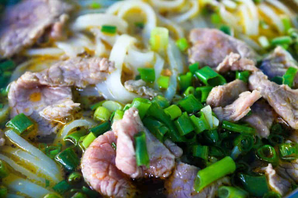 Close-up view of bowl of soup in Vietnam, with noodles, herbs, and sliced beef visible