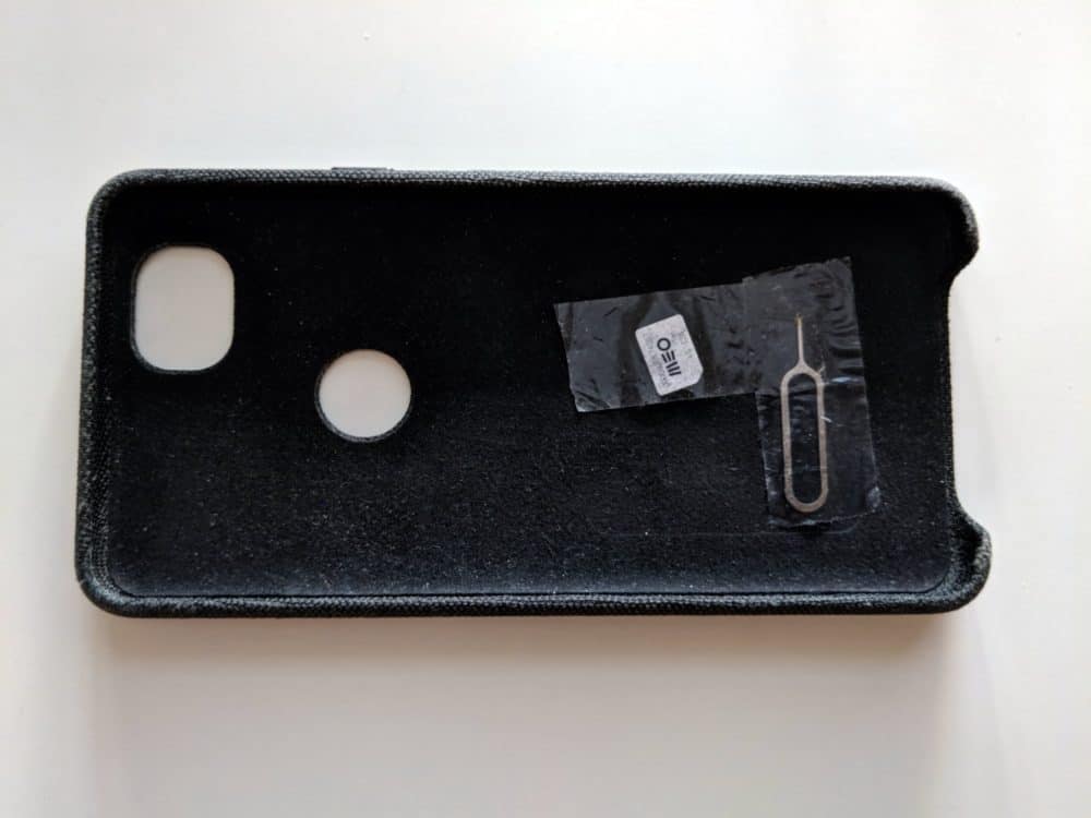 Phone case on white desk, with SIM card and SIM extractor extractor tool taped to the inside of the case