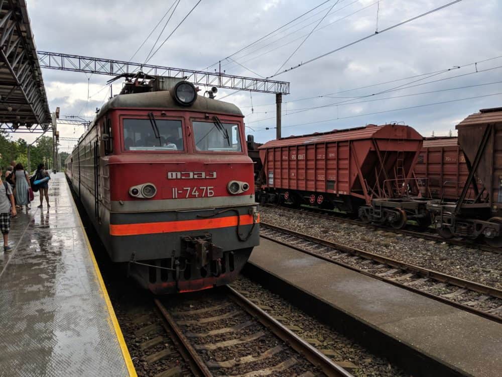 Train at a station in Georgia, with cloudy skies and a wet platform with a few people on it.