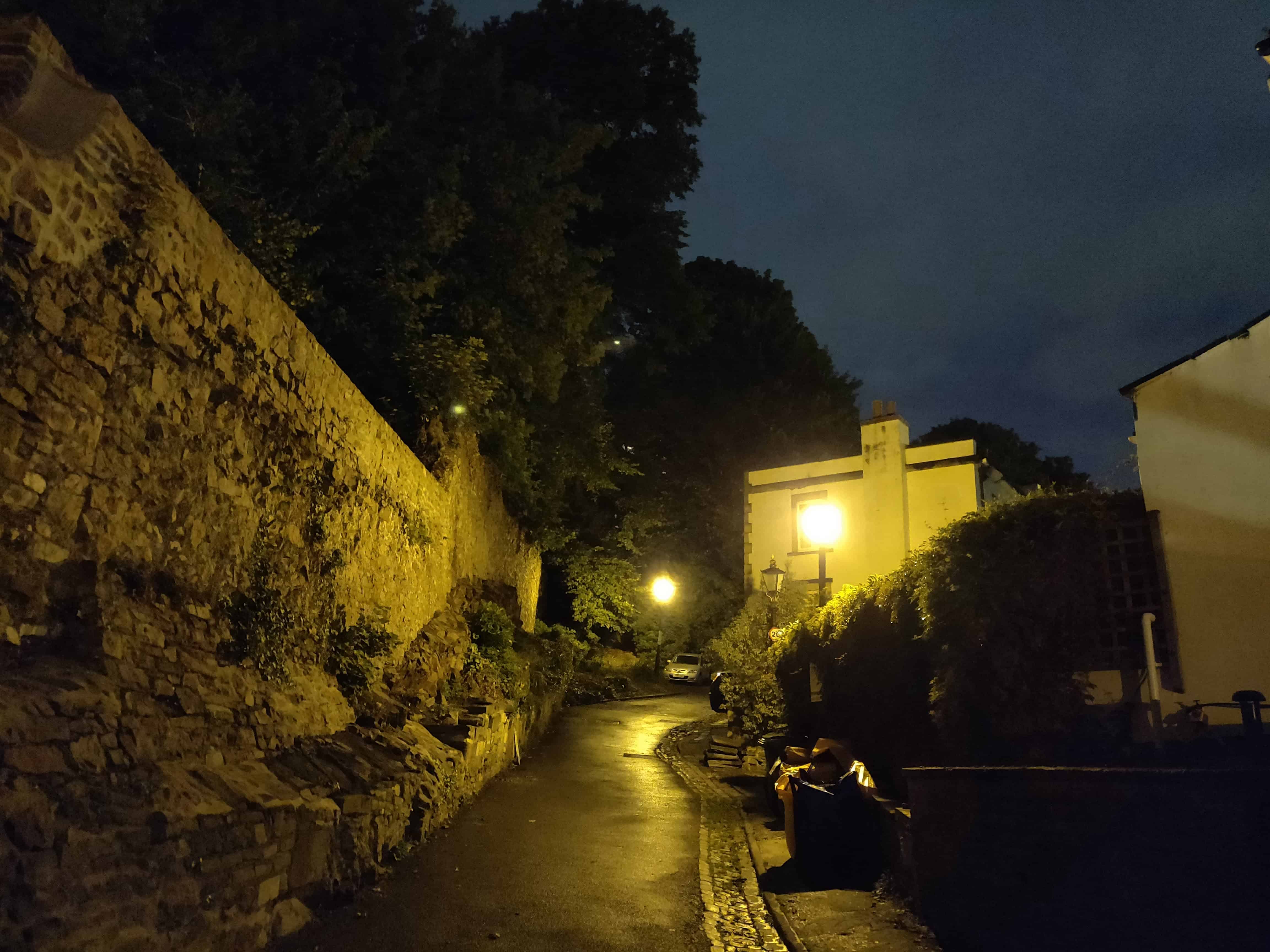 Alleyway at night, with a stone wall on one side and open on the other.