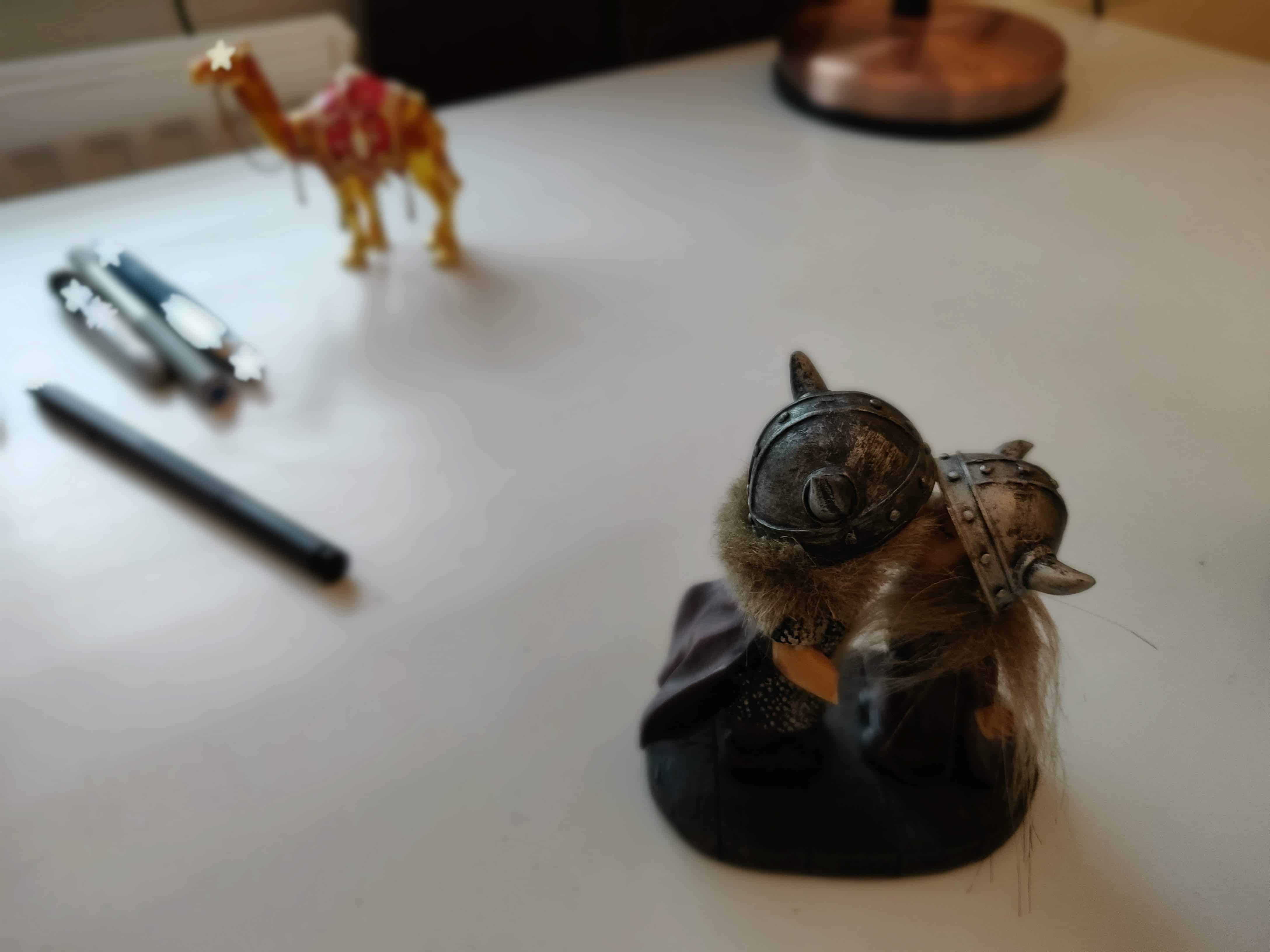 Figurine on a desk of two trolls kissing, with blurred pens and other items on the desk behind. White stars overlaid on pens and camel figurine.