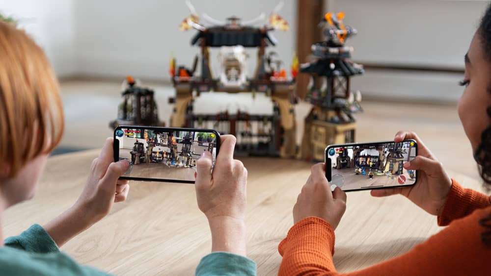 Two people holding iPhones in front of them landscape orientation, taking a photo of Lego sculpture. 