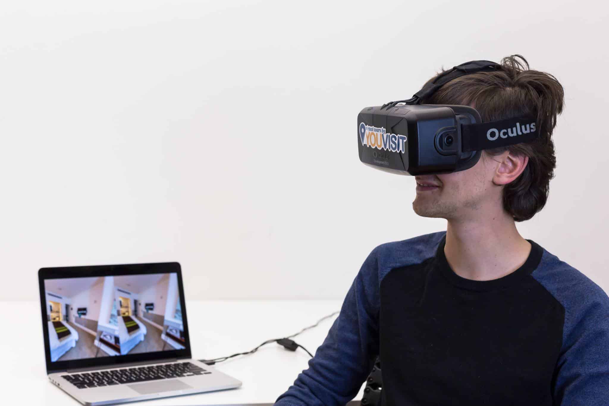 Man wearing a VR headset in a white room with a laptop alongside