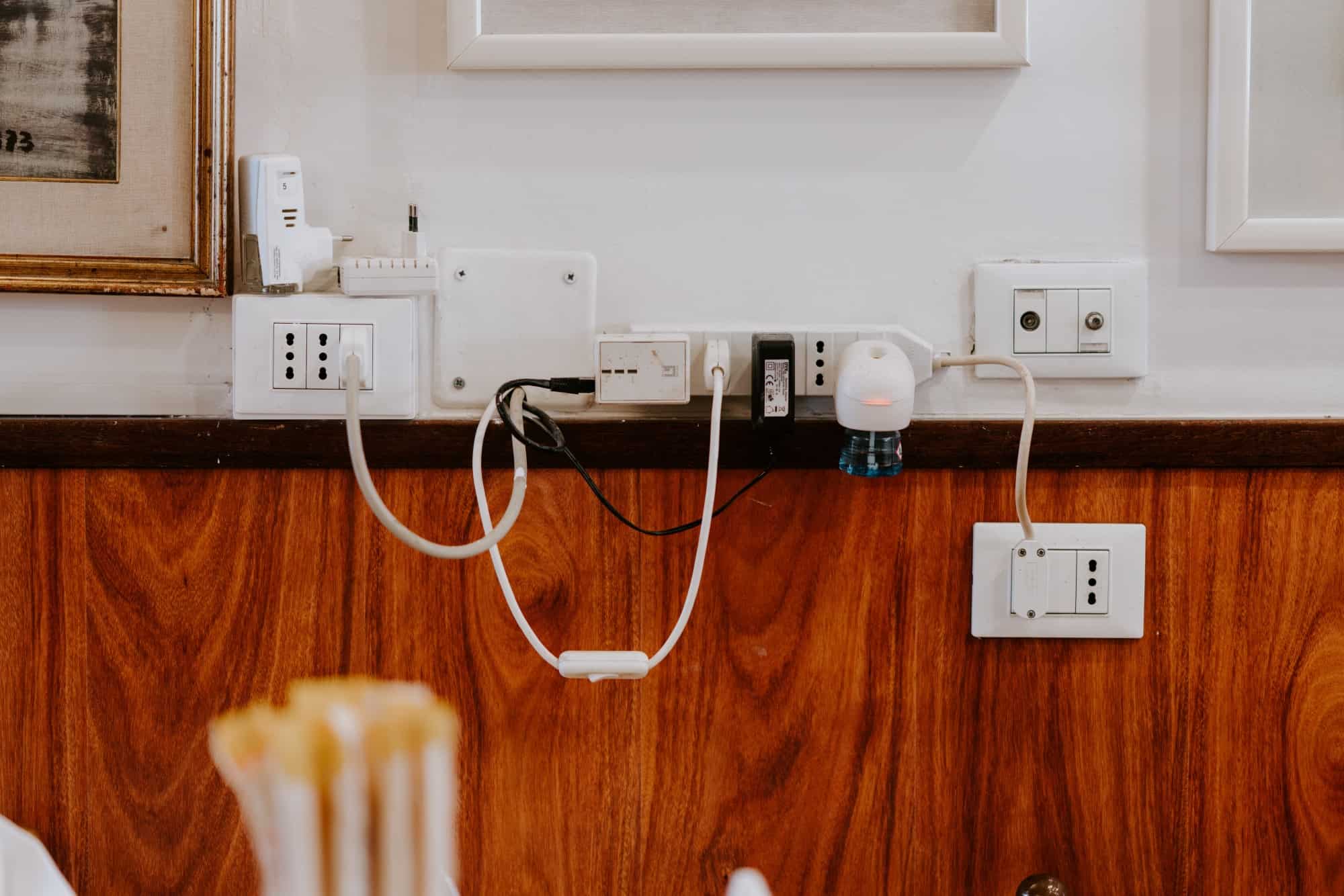 Several gadgets and sockets on white wall, connected by a range of different cables
