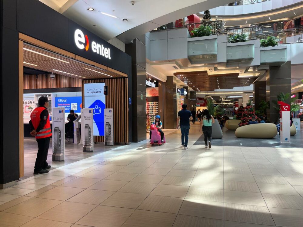Outside of an Entel phone store in a shopping mall in Santiago, Chile, A security guard is standing in the doorway, and customers can be seen walking around nearby.