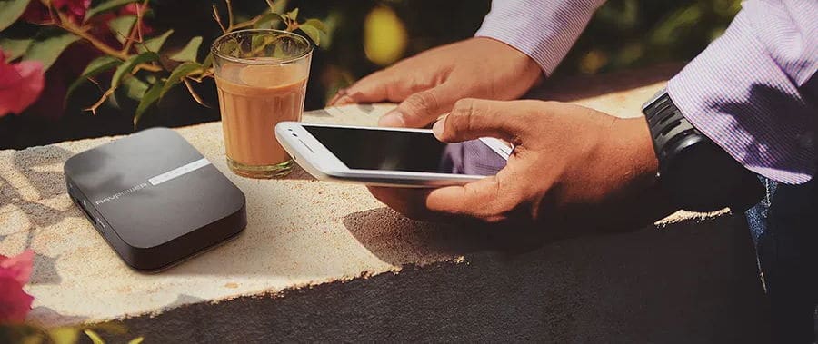 Person holding phone above a Ravpower FileHub device sitting beside a glass of juice