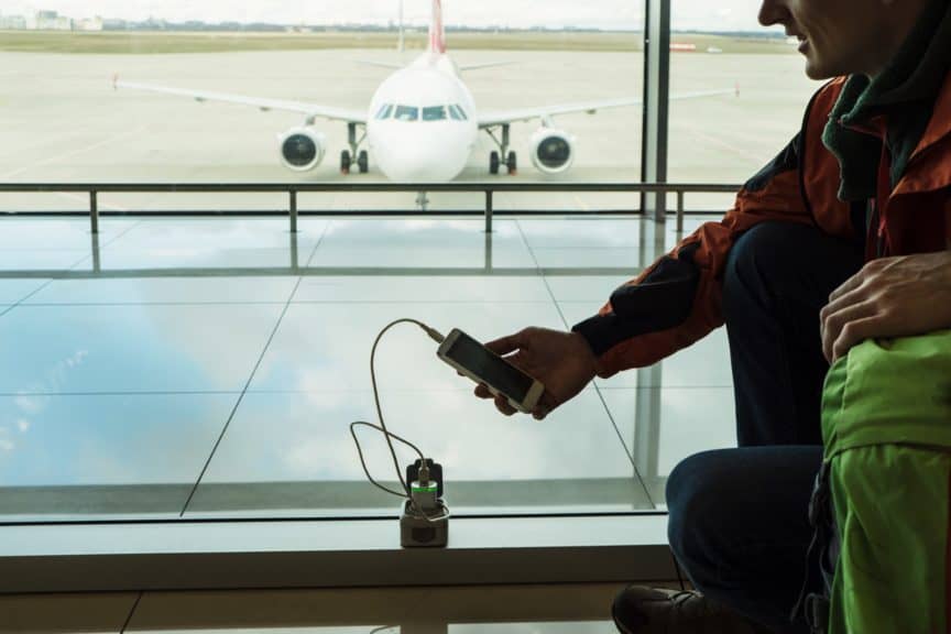Man at airport using travel power adapter to charge phone