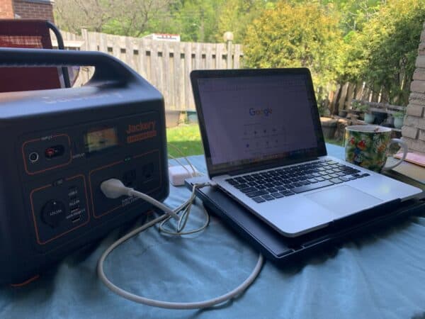 Laptop plugged into portable electric generator on a table overlooking a backyard.