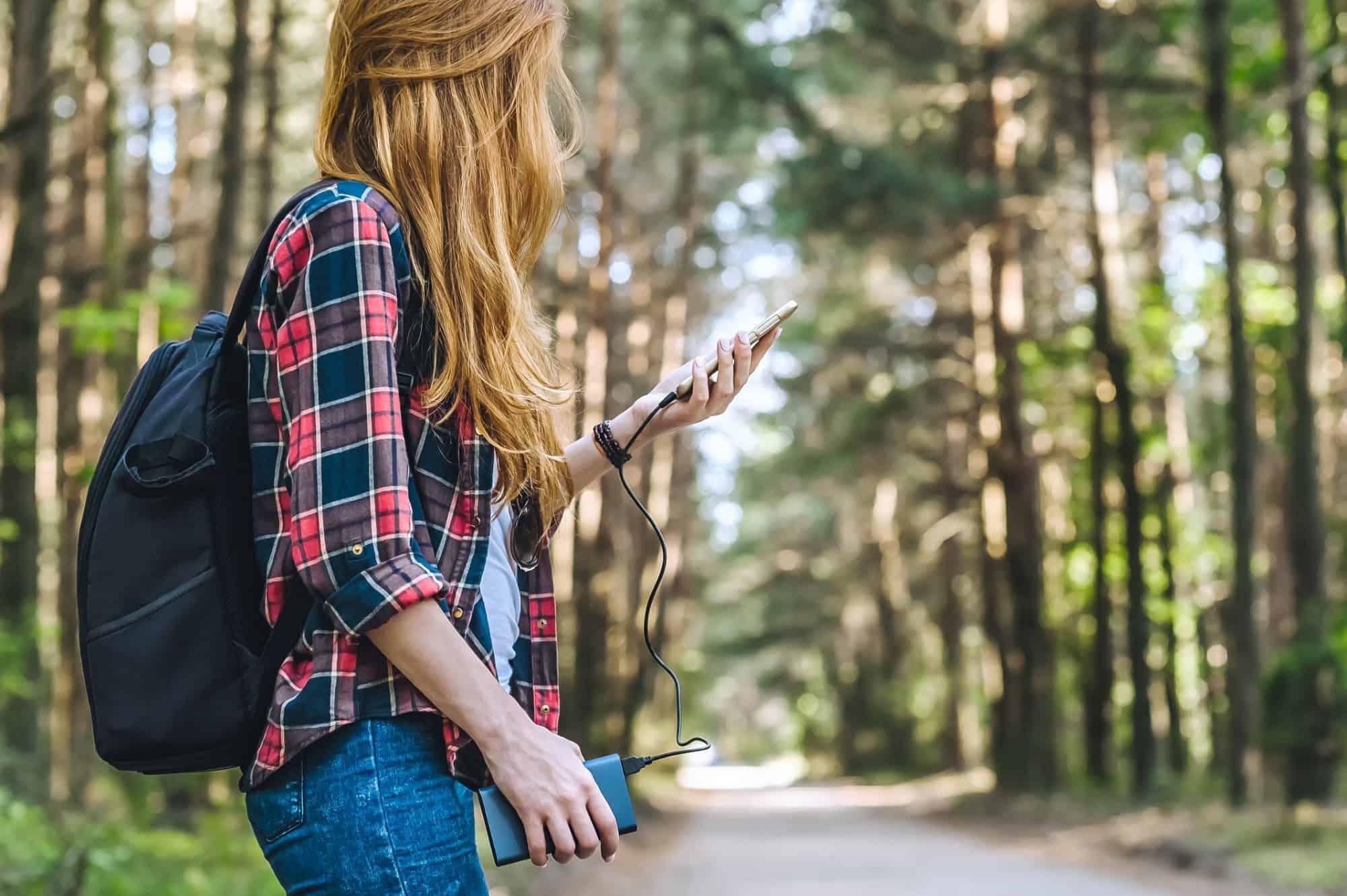 Woman charging phone from power bank in forest