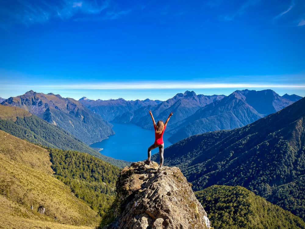 Lauren Juliff with arms in the air while walking the Kepler Track in New Zealand