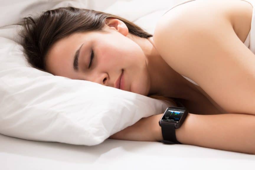 Woman sleeping on bed wearing smartwatch showing heartbeat monitor