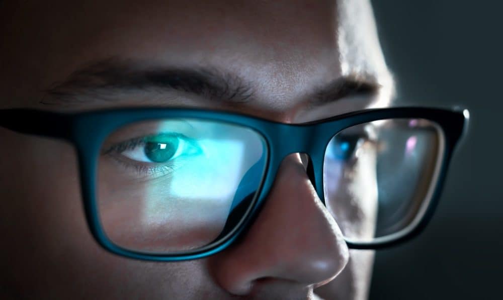 Close-up of man wearing glasses with reflection of computer screen