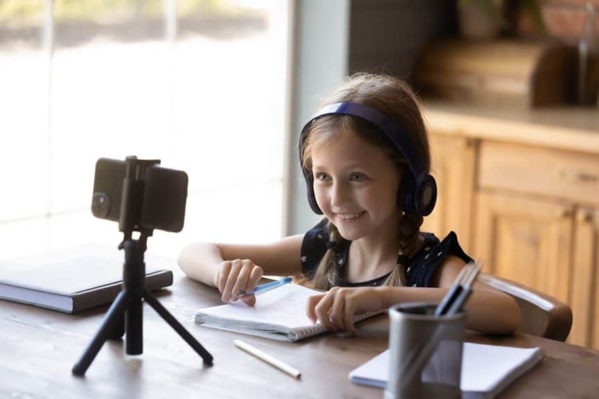 Young girl wearing headphones while looking at phone on tripod