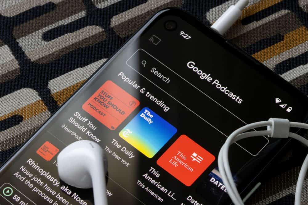 Closeup of smartphone showing Google Podcasts app, with a set of earbuds on top