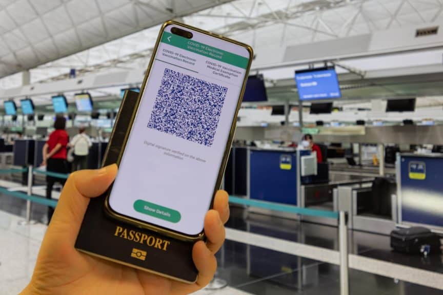 Person near check-in desks holding phone displaying Covid-19 vaccination app