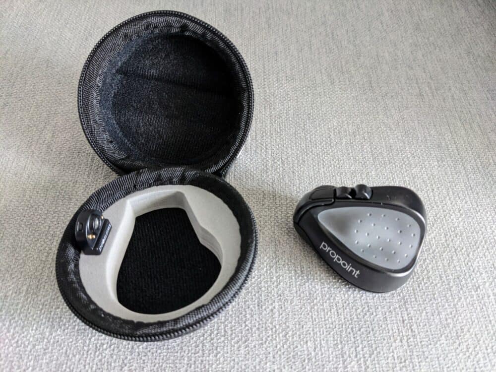 View of Swiftpoint ProPoint mouse sitting beside its open travel case, on plain fabric
