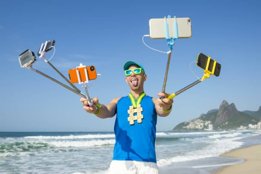 Man standing on beach holding several selfie sticks in front of him