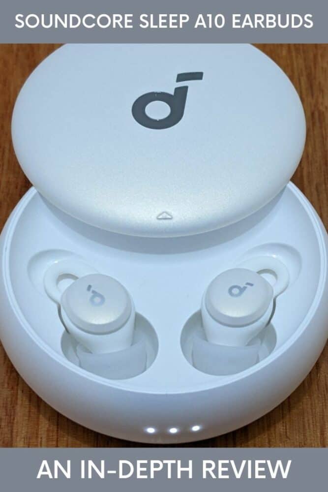 Round white Soundcore Sleep A10 earbuds case on a wooden table, with both earbuds inside the case and the charging lights on the front illuminated. Text "Soundcore Sleep A10 earbuds" at top and "An In-Depth Review" at bottom