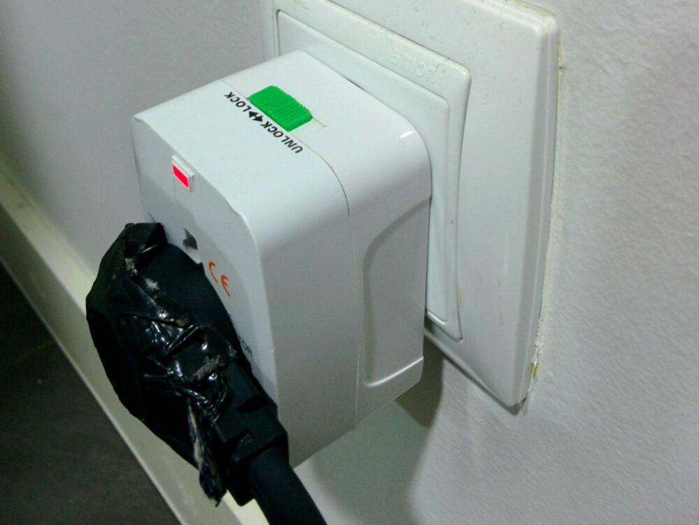 CyonGear universal travel adapter inserted into wall outlet with duct-taped plug inserted into it