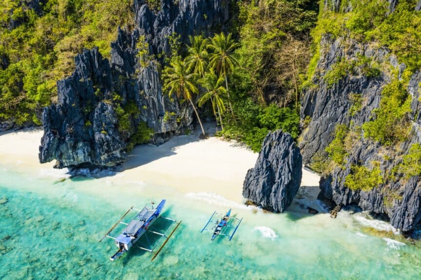 Outrigger boat on beach in Palawan, Philippines, with limestone cliffs behind