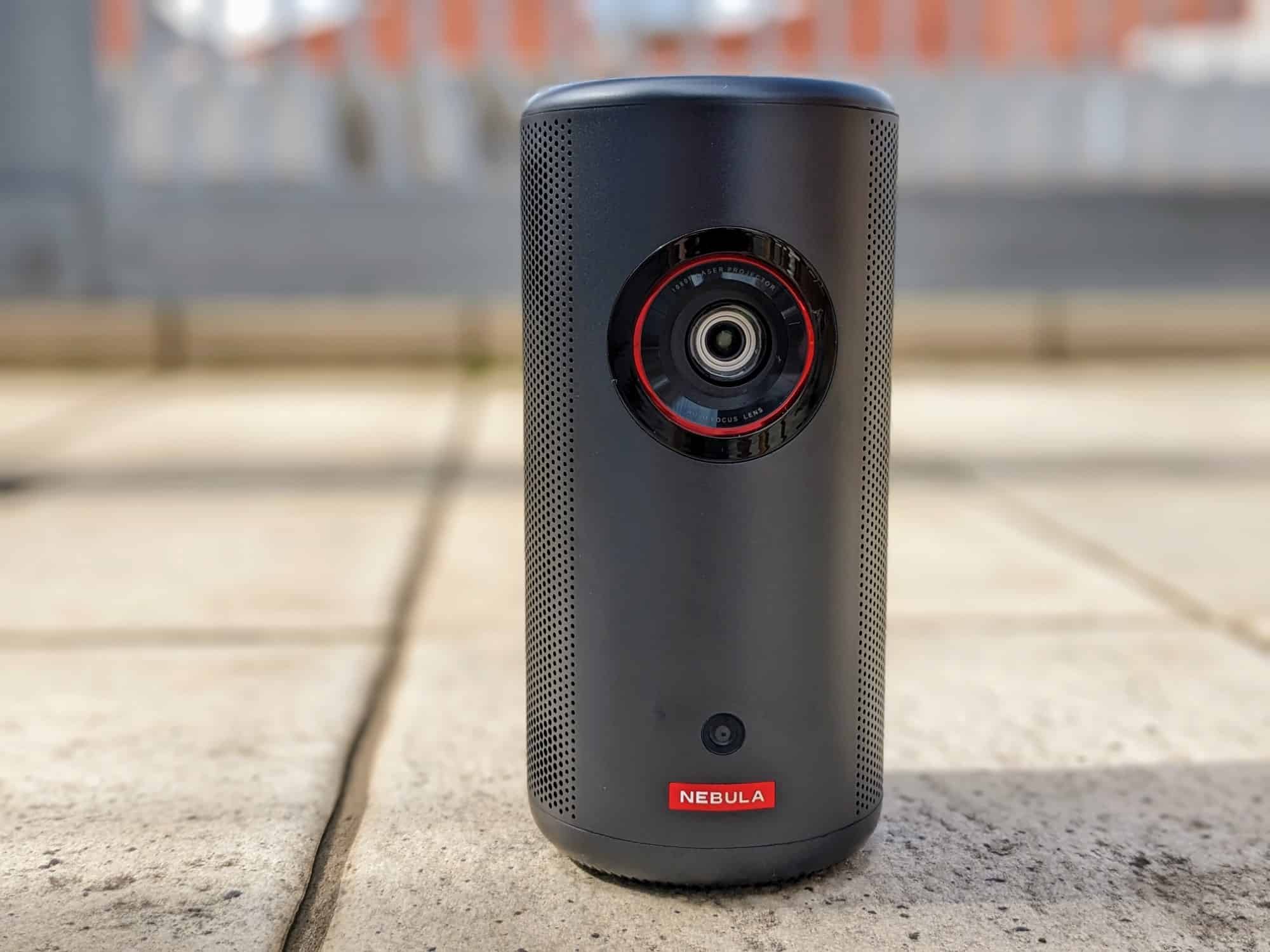 Nebula Capsule 3 Laser projector on stone tiles with blurred metal fence in background