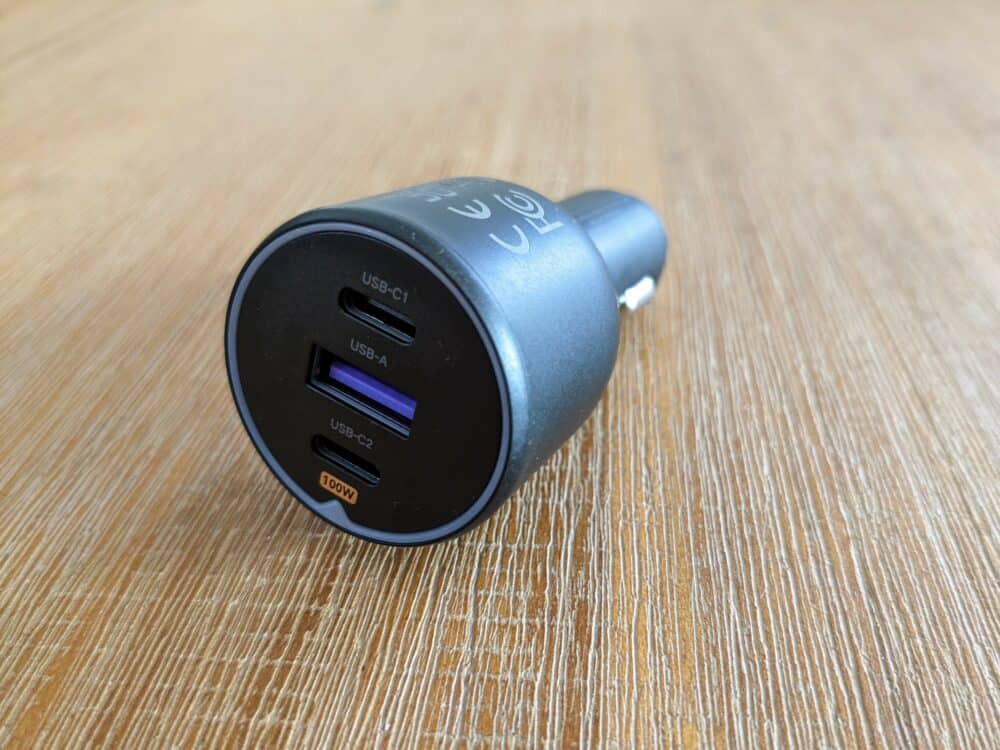 USB car charger sitting on wooden table. Charger has two USB C ports, above and below a USB-A port.