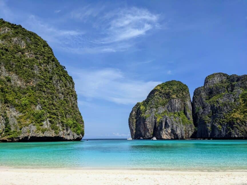 Photo taken from the beach at Maya Bay, Thailand, looking out towards large limestone karsts and gap to the ocean, with blue skies