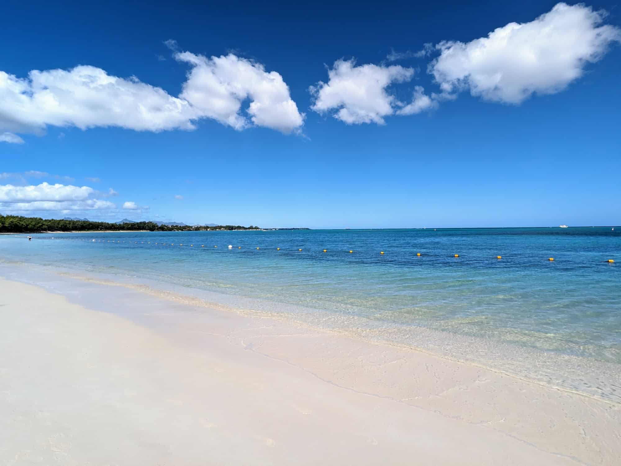 Beach and ocean in Mauritius, with small swimming buoys visible in foreground and a few puffy white clouds in blue sky
