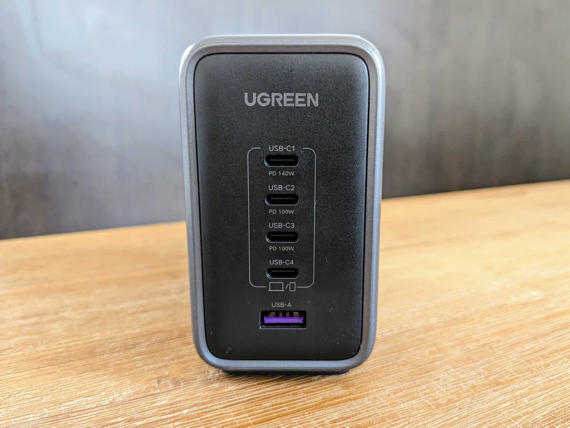 Ugreen 300W desktop charger sitting on wooden table, with darker wood counter behind. Front of charger visible with five USB ports and Ugreen branding at top.
