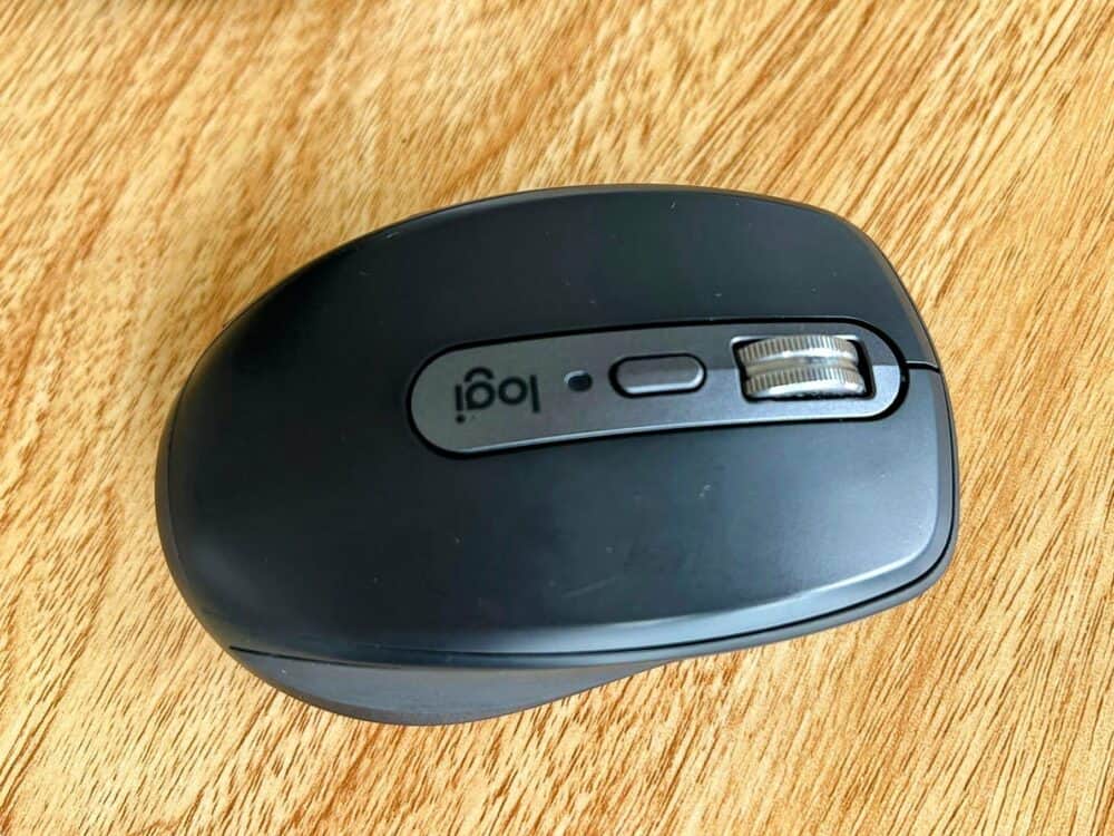 Closeup of a black mouse on a wooden desk with "logi" (upside down) in the middle of the mouse