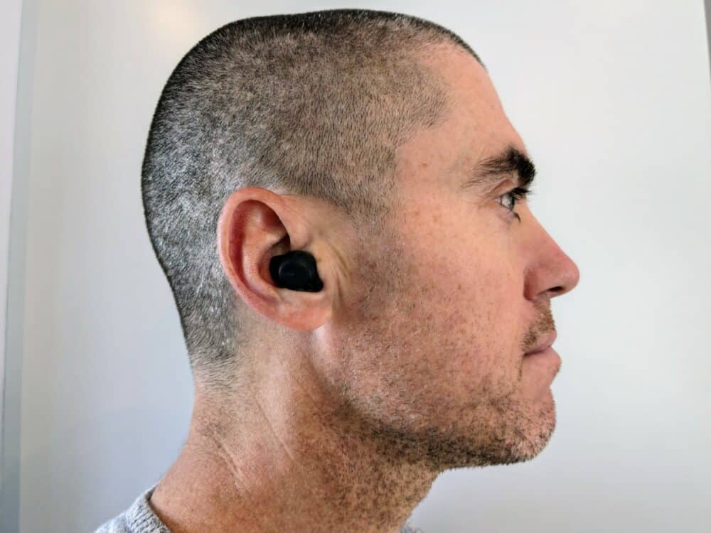 Side view of man with short hair and stubble wearing a small black earbud in his right ear.