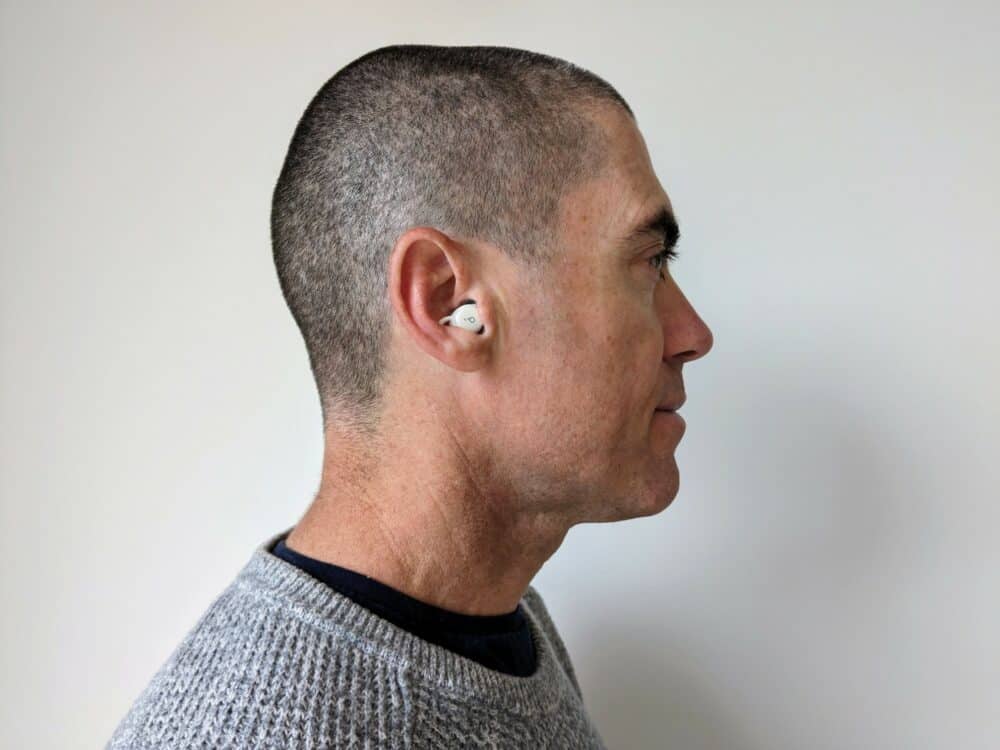 Side view of man in grey sweater and blue t-shirt with a small white earbud in his right ear