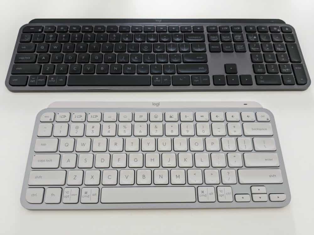Two keyboards, one in front of the other. The front one is black and larger than the back one, with a number pad on the right hand side. The lower one has no number pad and is grey in color.