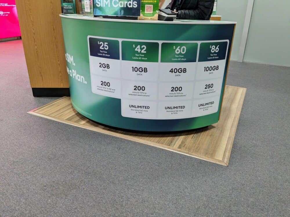 Small counter advertising pricing for One NZ SIM cards at an airport.