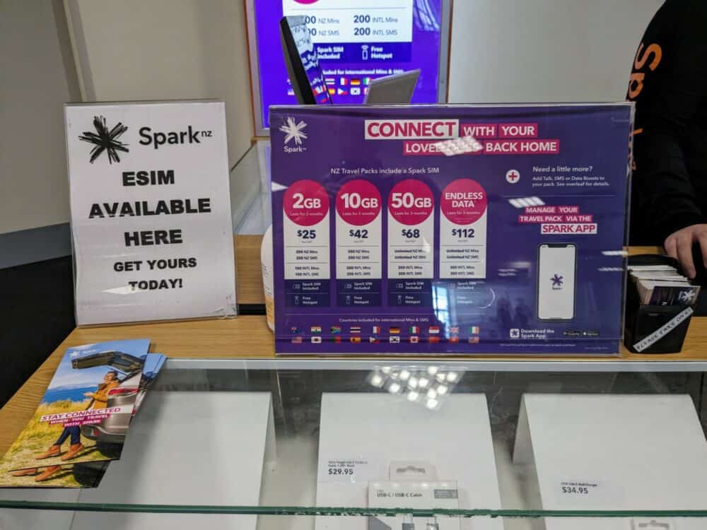 Sign on a glass-topped counter advertising Spark's travel SIM pricing, with options from 2GB to Endless Data. A smaller sign on the left advertises the availability of an eSIM