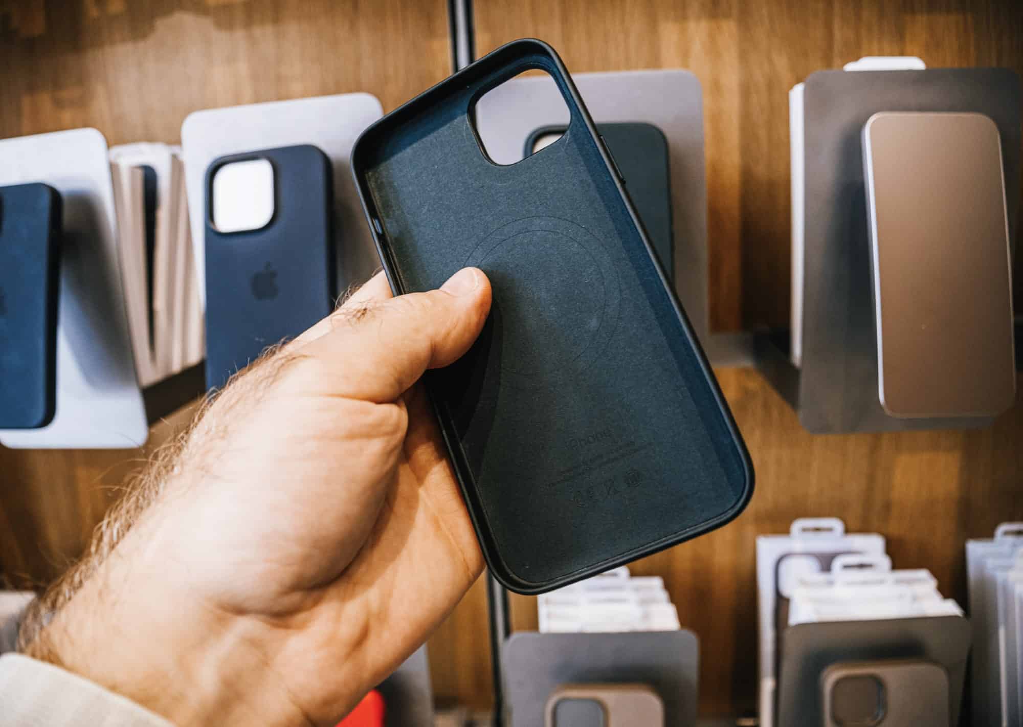 Male hand holding empty iPhone 15 case in front of a wall of similar display cases