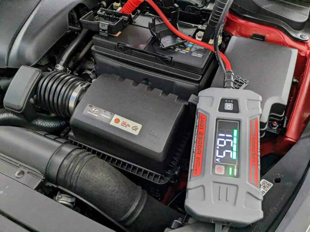 Lokithor J401 portable jump starter with leads connected to car battery. 16.5v measurement visible on display.