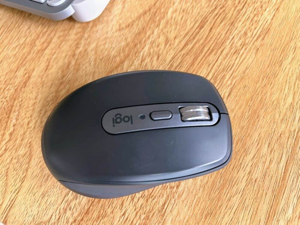 MX Anywhere 3S mouse on wooden table with small section of keyboard visible at top left