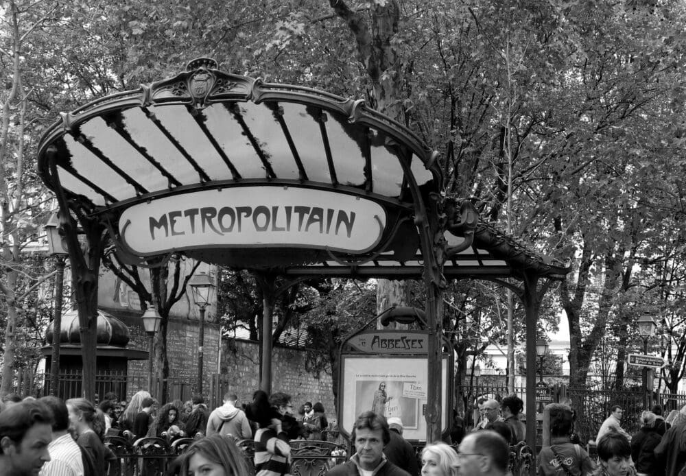 Paris metro station entrance and sign with crowds of people walking nearby.