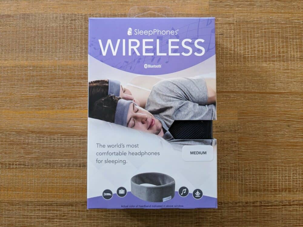 Rectangular box on wooden table with heading reading "SleepPhones Wireless" at top, a picture of two people lying in bed wearing sleep headbands below, and text saying "The world's most comfortable headphones for sleeping" below.