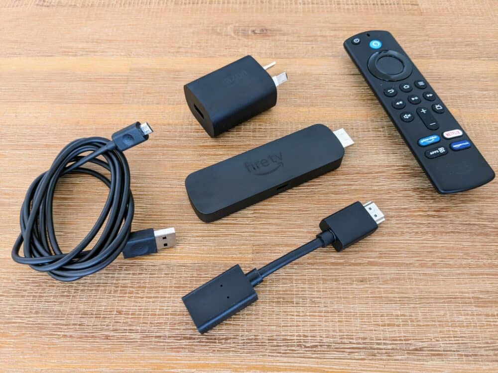 Amazon Fire TV Stick, remote control, wall charger, power cable, and HDMI extender on wooden table