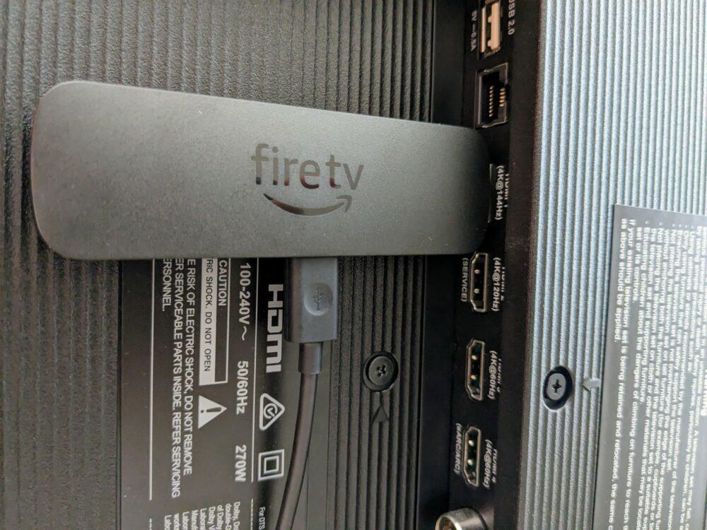 Amazon Fire TV Stick  connected to HDMI port of television with power cable inserted at bottom of stick