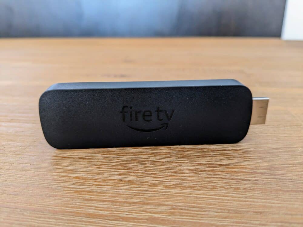 Amazon Fire TV Stick  sitting upright on one of the long edges, on a wooden table