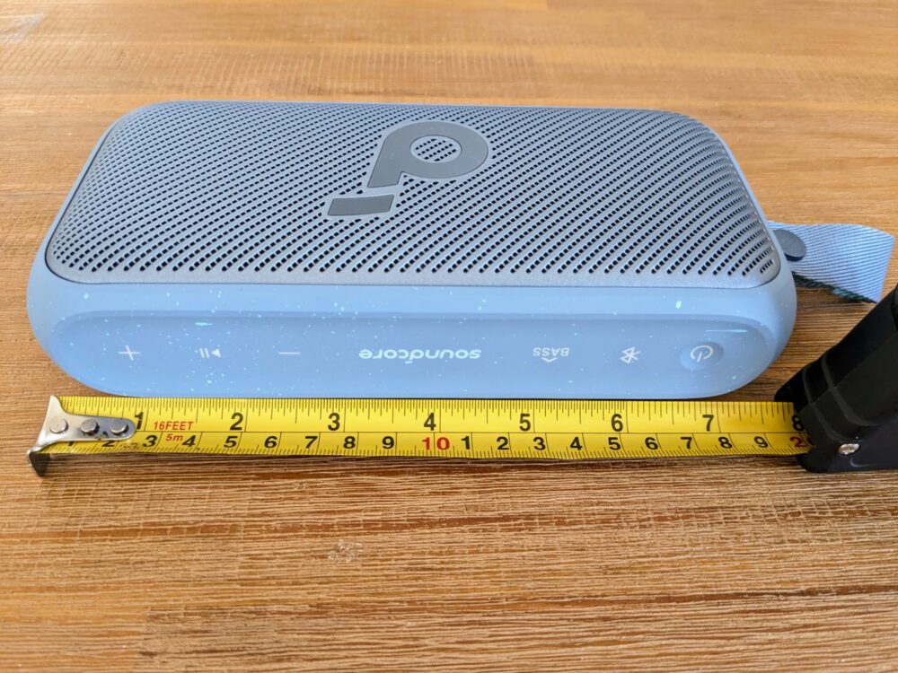 Portable speaker lying on a wooden table with a tape measure laid out alongside.