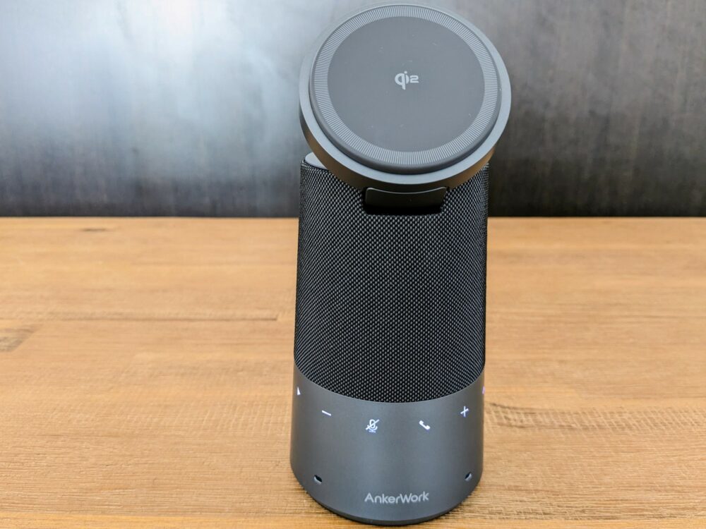 Front-on view of a cylindrical speakerphone on a wooden table, with a circular section on top that's angled towards the front