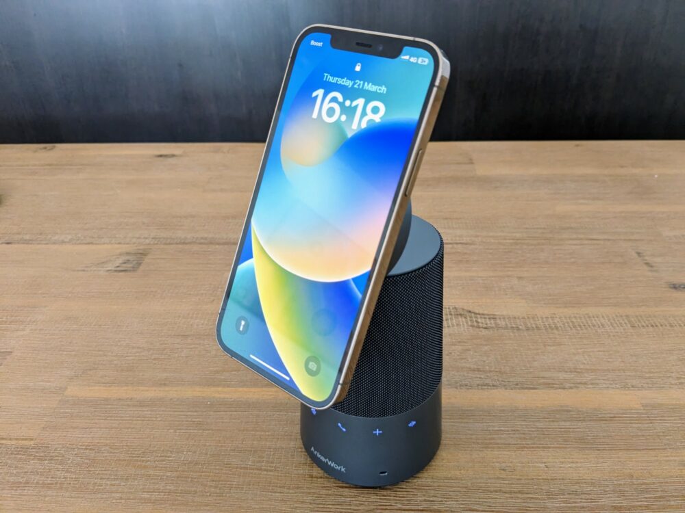 AnkerWork speakerphone sitting on a wooden table, with an iPhone magnetically attached to a stand on top.